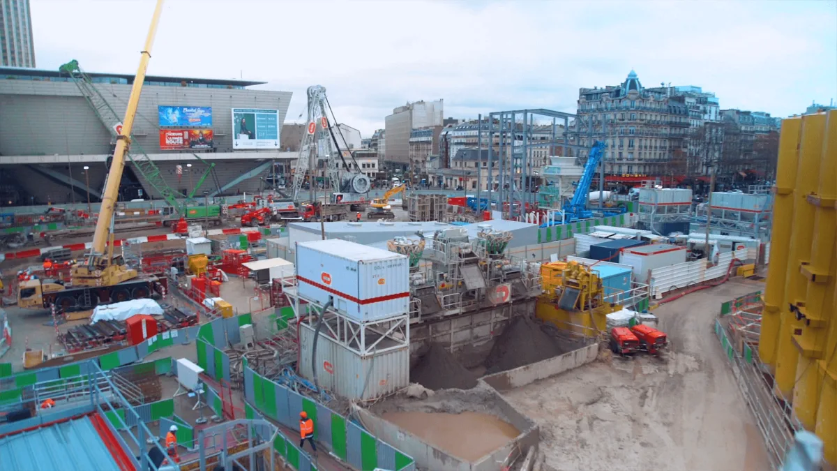 Construction site with cranes, excavation, safety barriers, and equipment coordination