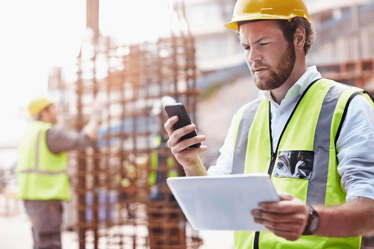 Construction supervisor using smartphone and tablet for on-site management and safety