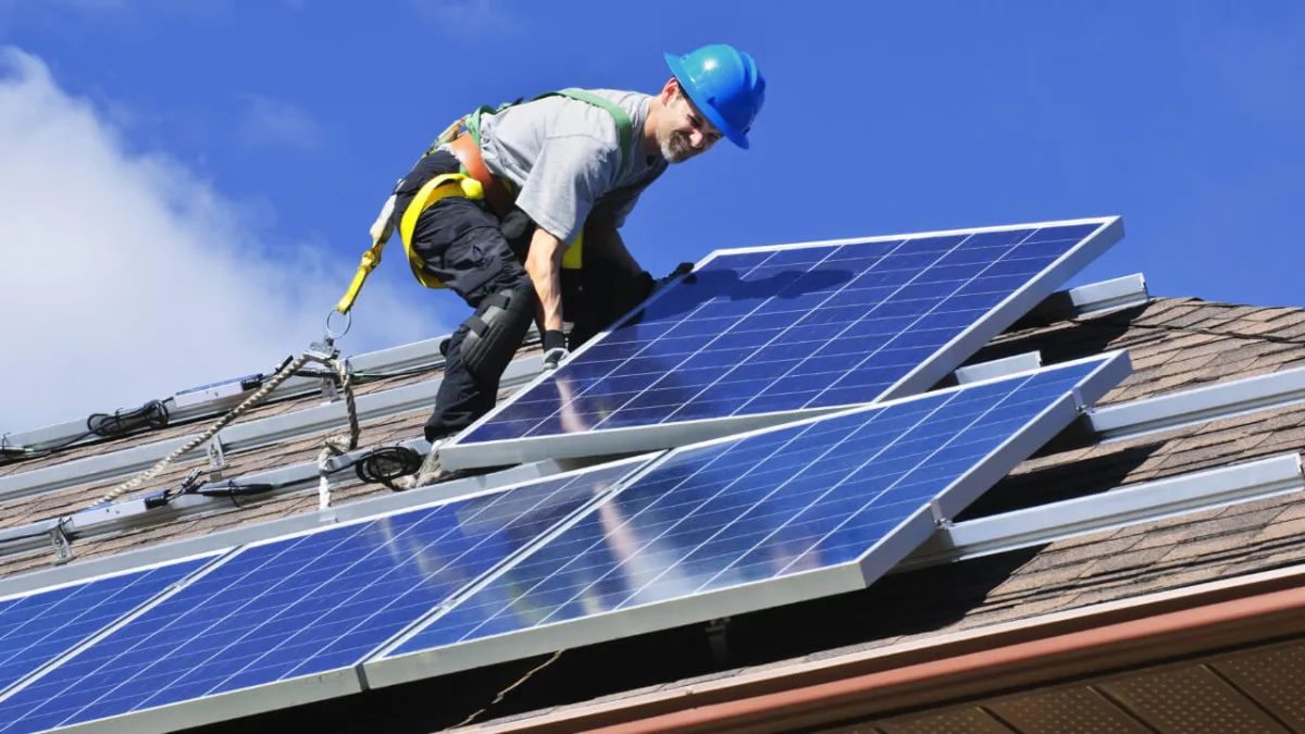 Professional installing solar panels on residential roof with safety harness and hard hat