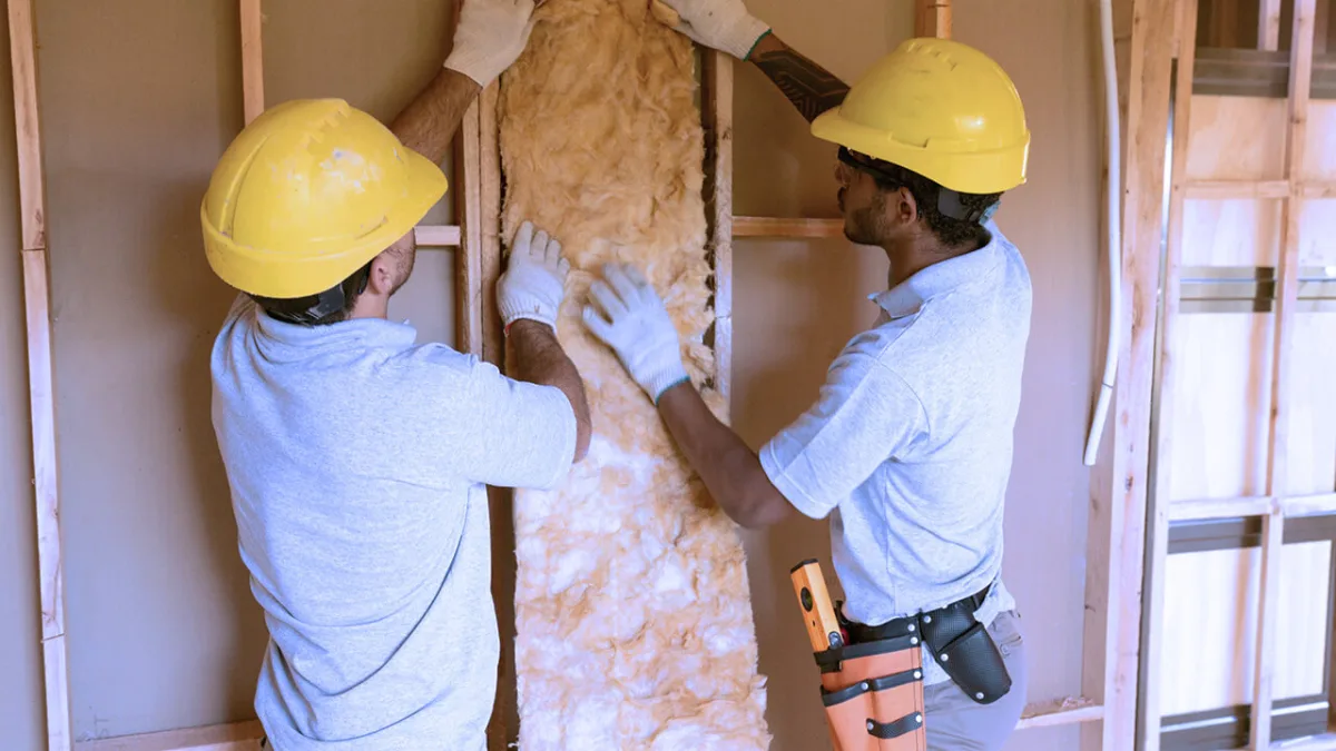 Workers installing insulation between wall studs on construction site