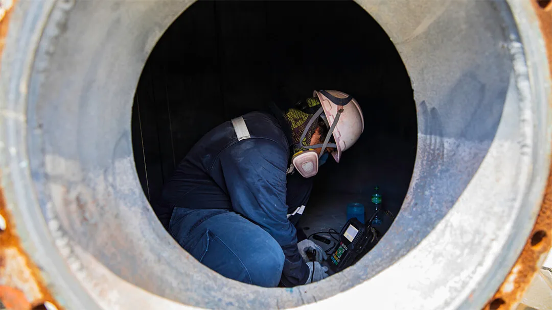 Site worker in full safety gear performing confined space tunnel inspection
