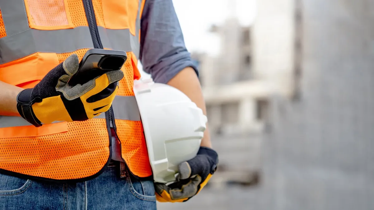 Construction worker in reflective vest using mobile device for site safety