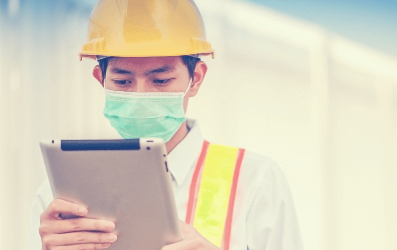 Construction worker with mask and hard hat using tablet for site safety