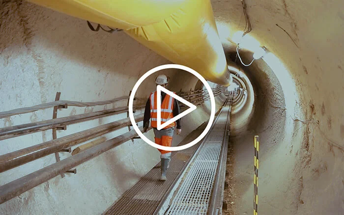 Worker in safety gear inspecting underground infrastructure pipeline in construction tunnel