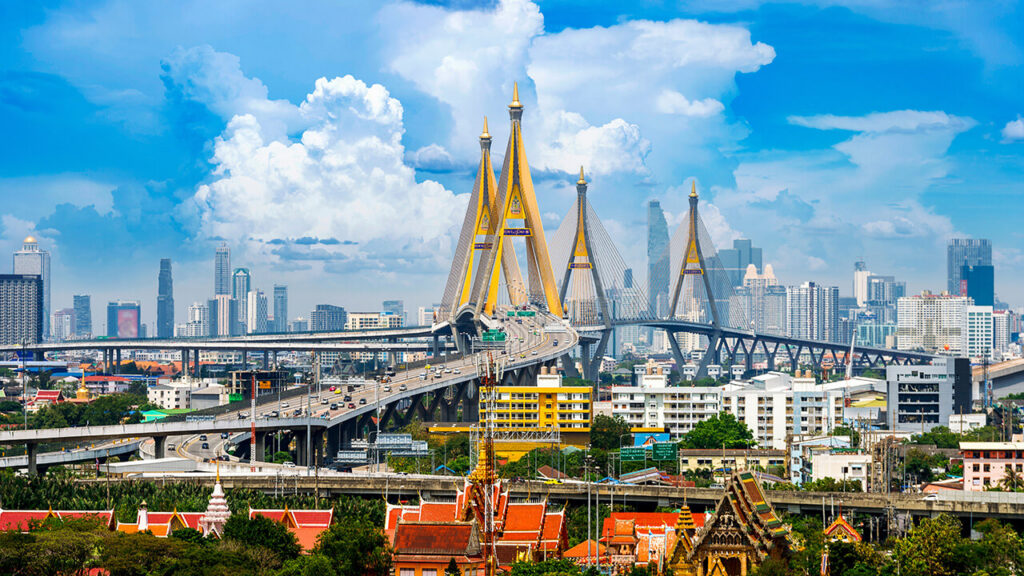 Large cable-stayed bridge under construction with cranes in Bangkok cityscape