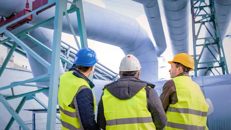Three workers inspect a petrochemical facility's pipeline systems in safety gear