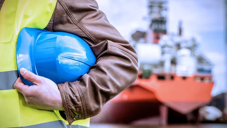 Site safety inspector holding blue hard hat at shipbuilding facility